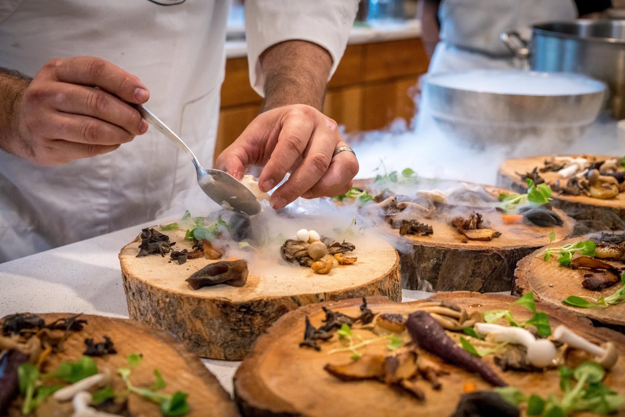 Contact A chef artfully plating a gourmet dish with mushrooms and greens on wood slices.