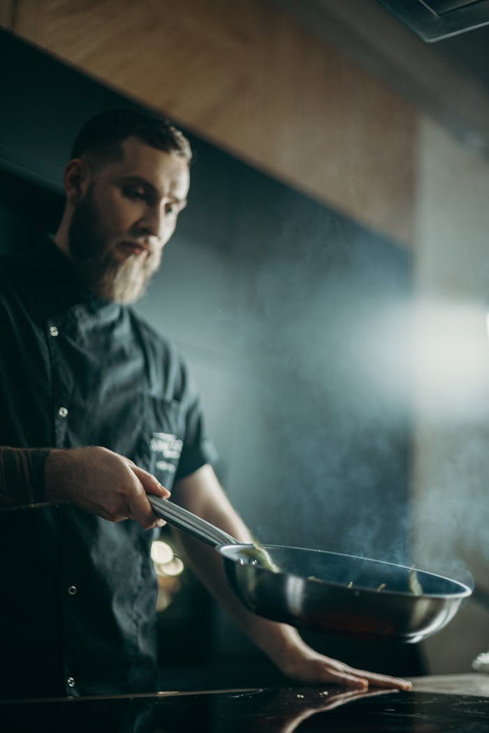 Services A focused chef prepares a meal using a frying pan in an indoor kitchen setting.