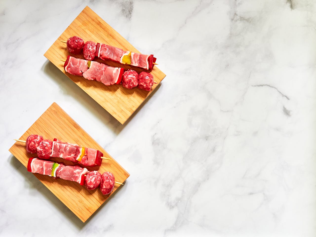 Top view of raw meat skewers on wooden boards ready for grilling, emphasizing freshness and preparation.